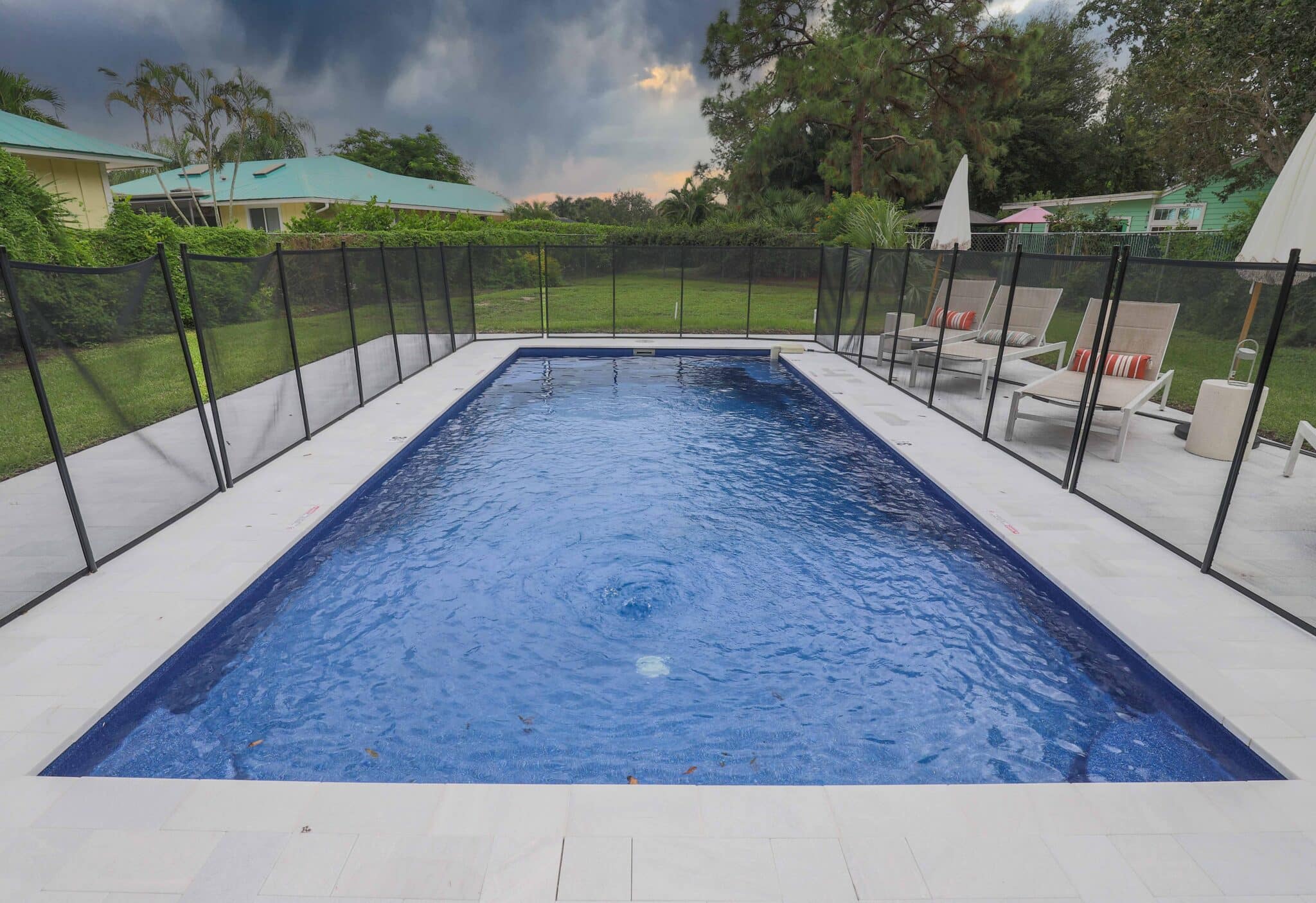 Completed rectangular fiberglass pool in Jupiter with a light-colored deck, mesh pool fence, and lounge seating.