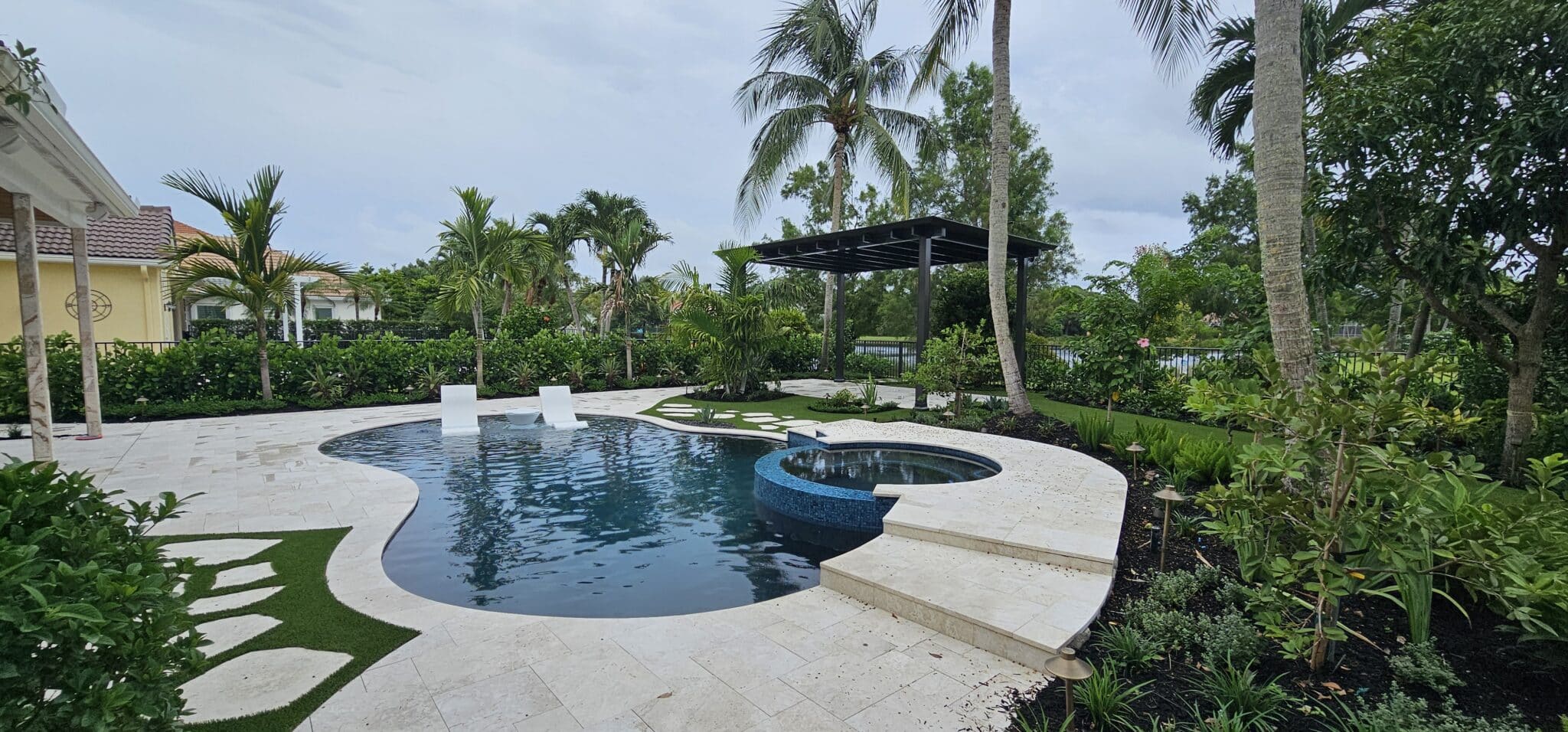 Freeform swimming pool with attached round spa, light deck and tropical landscaping in Palm Beach Gardens